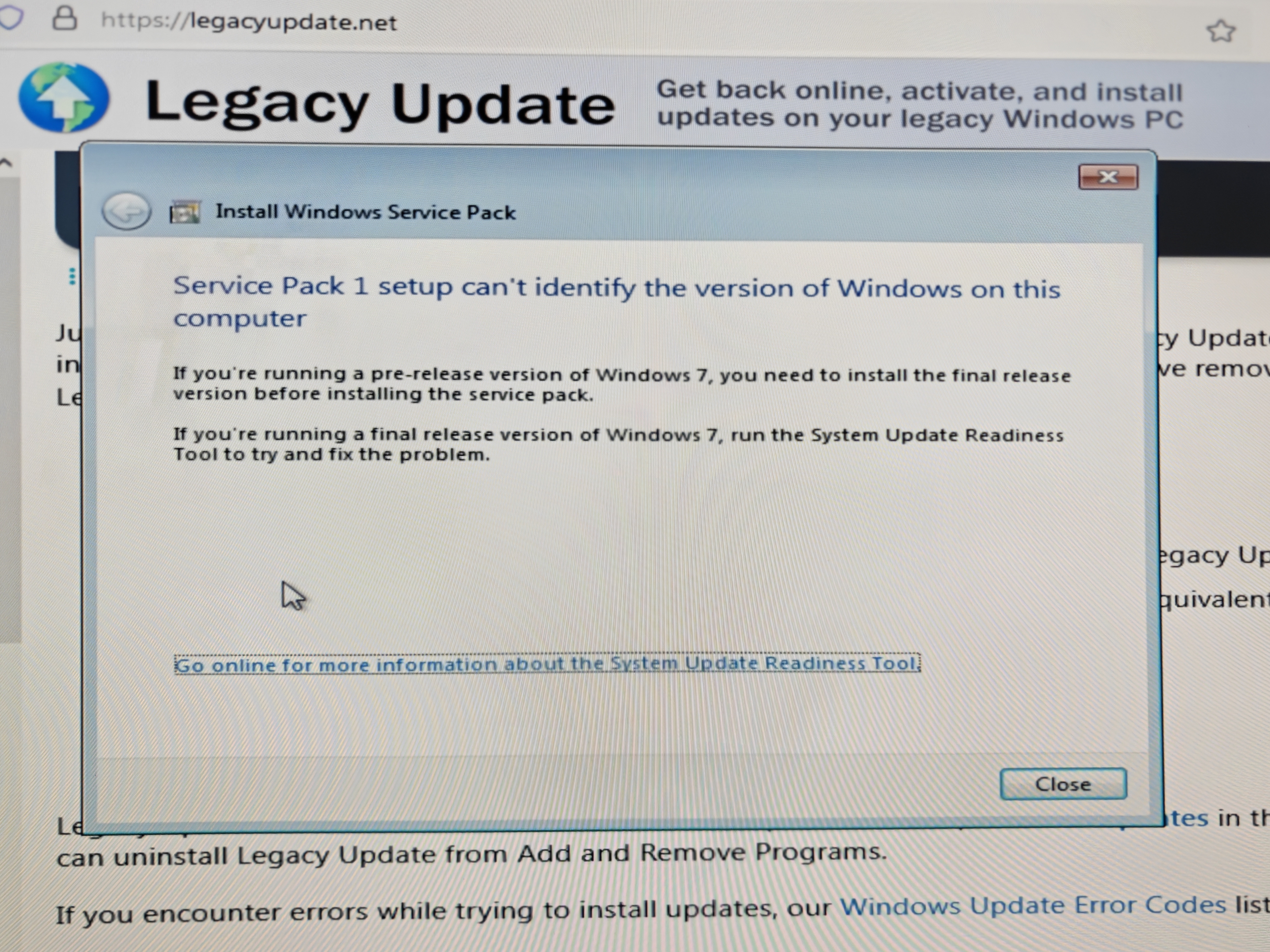 The installer for Windows 7 Service Pack 1 is in the foreground, overlaid on IE8 which is open on legacyupdate.net. The installer shows the following error: Service Pack 1 setup can&rsquo;t identify the version of Windows on this computer. If you&rsquo;re running a pre-release version of Windows, you need to install the final release version before installing the service pack. If you&rsquo;re running a final release version of Windows 7, run the System Update Readiness Tool to try and fix the problem.